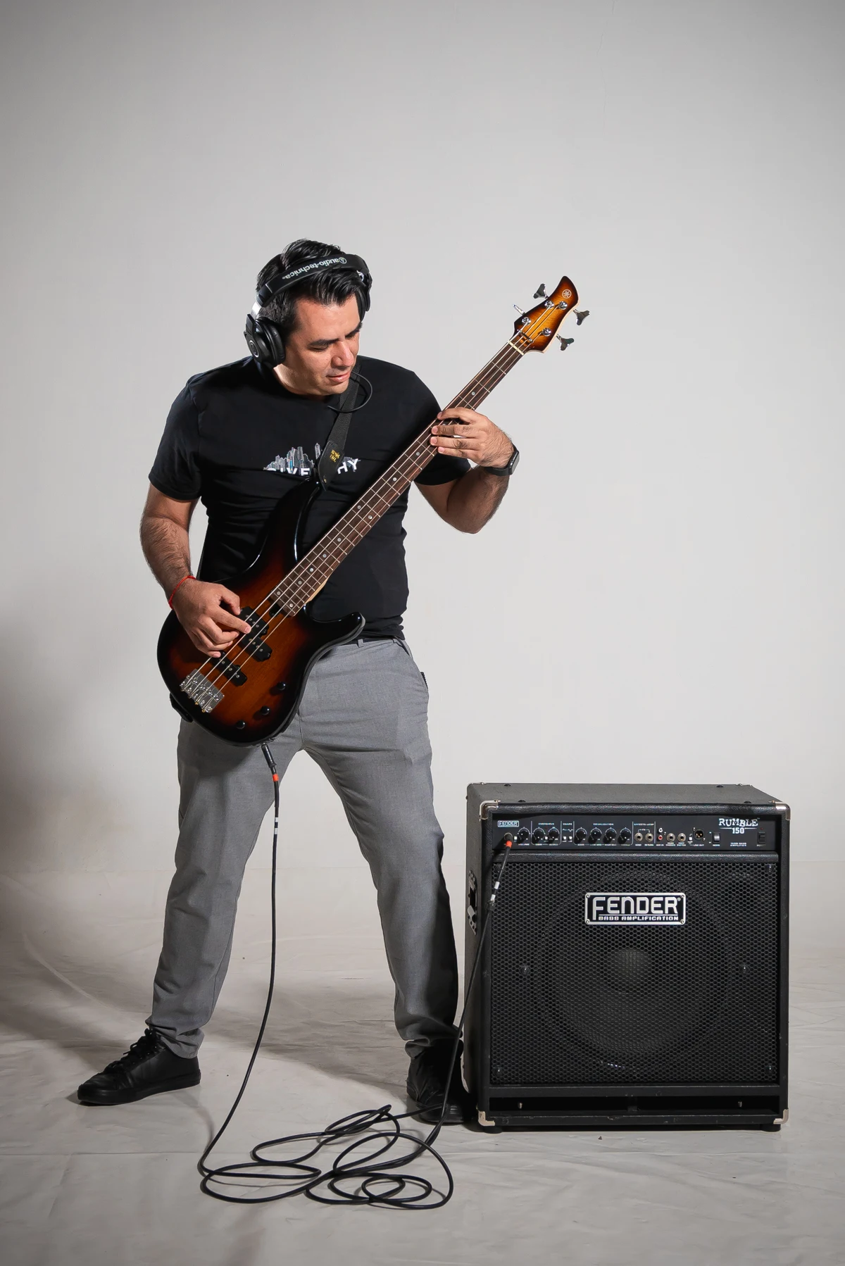 Músico tocando el bajo con audífonos junto a un amplificador.