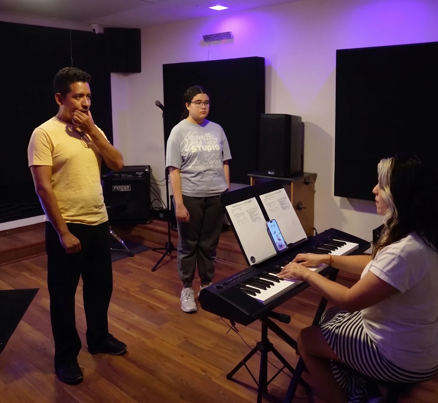 Clase de música con acompañamiento al teclado en un salón de ensayo.